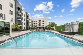 Sun-drenched pool area with a modern apartment building in the background at Bay Village 1 Apartment in Palmetto Bay, FL
